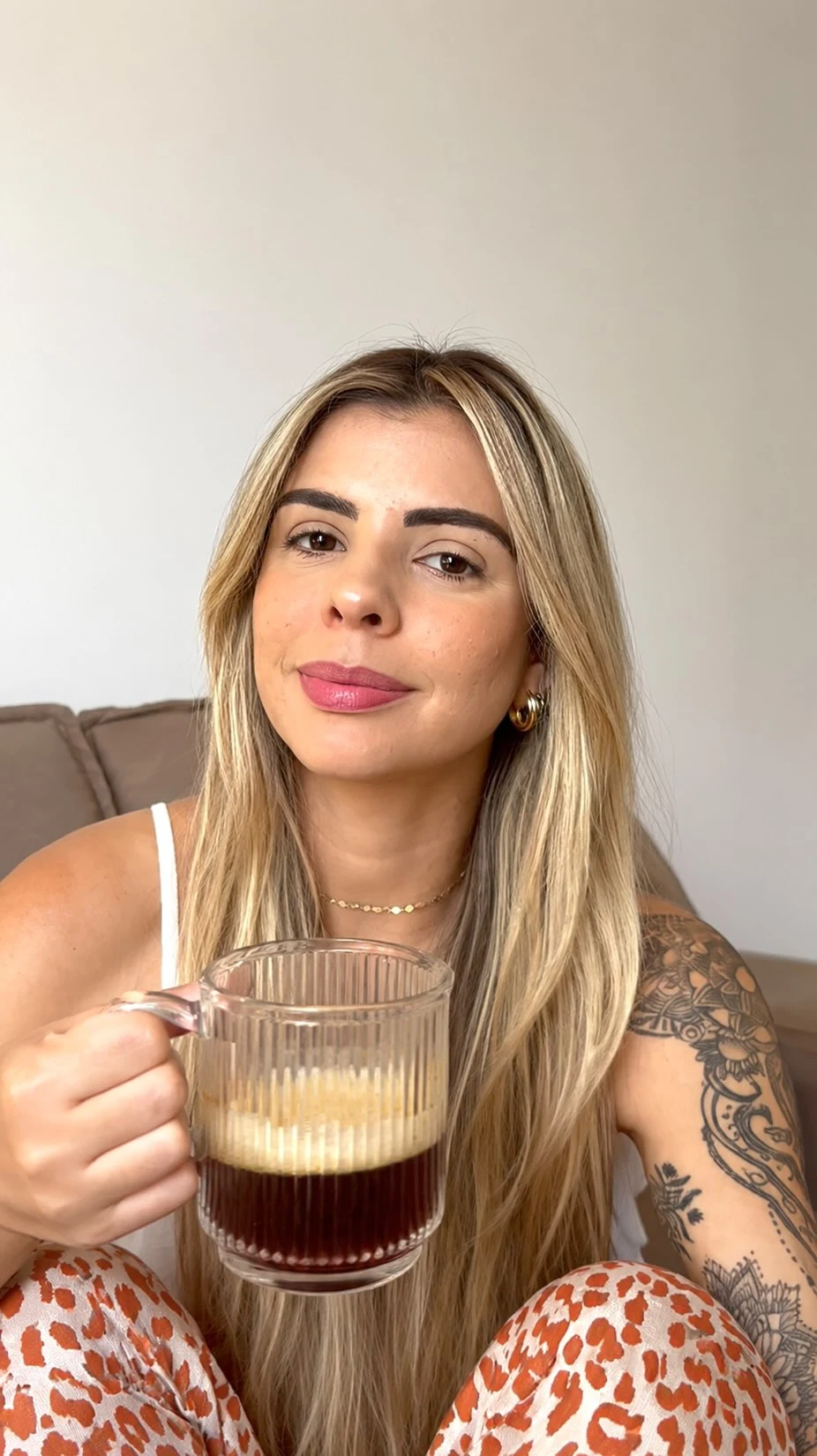 Rayssa com uma caneca de café em casa, de cabelo solto e blusa branca